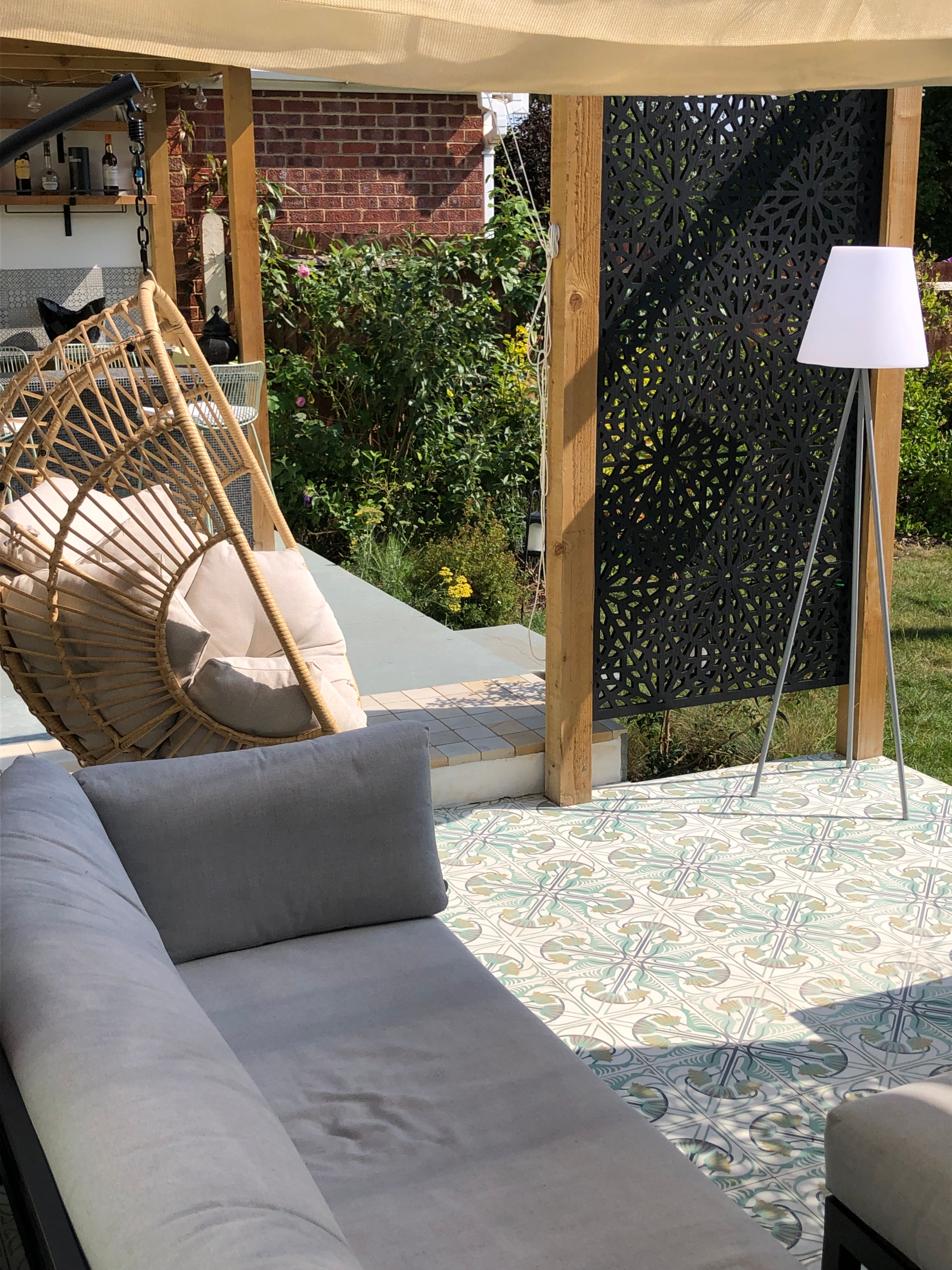 Relaxed seating under the pergola in a Bexley garden Bexley garden seating area with hanging chair, Jungle Bliss encaustic tiles and Moucharabiya screen under the pergola
