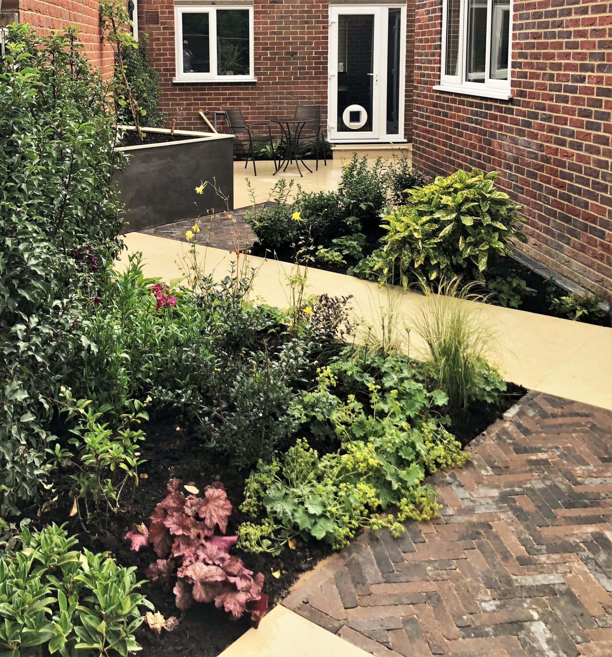 The finished layout in a Meopham garden Garden design in Meopham, Kent - diagonal Jura Beige paving, brick detail and layered planting leading to a seating area by the house