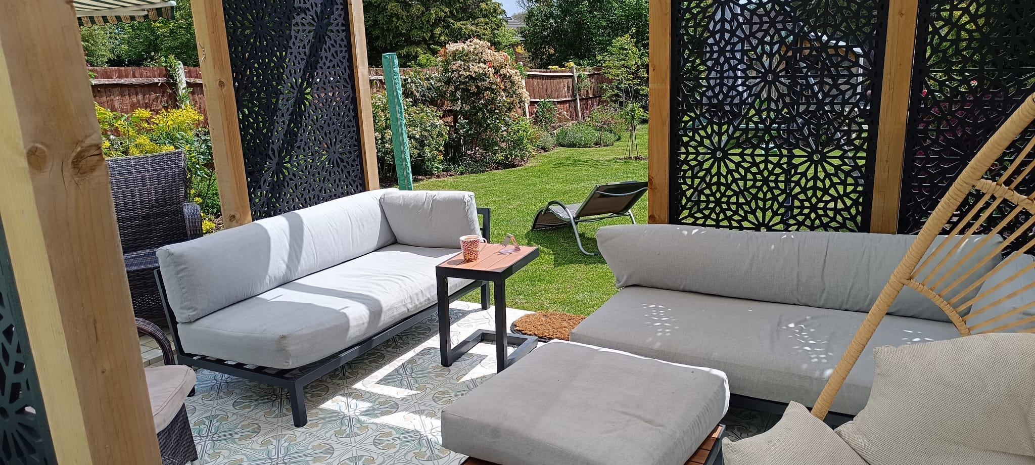 Covered pergola lounge in a Bexley garden Bexley garden pergola seating with sofas, Jungle Bliss encaustic tiles and Moucharabiya screens looking out to the lawn